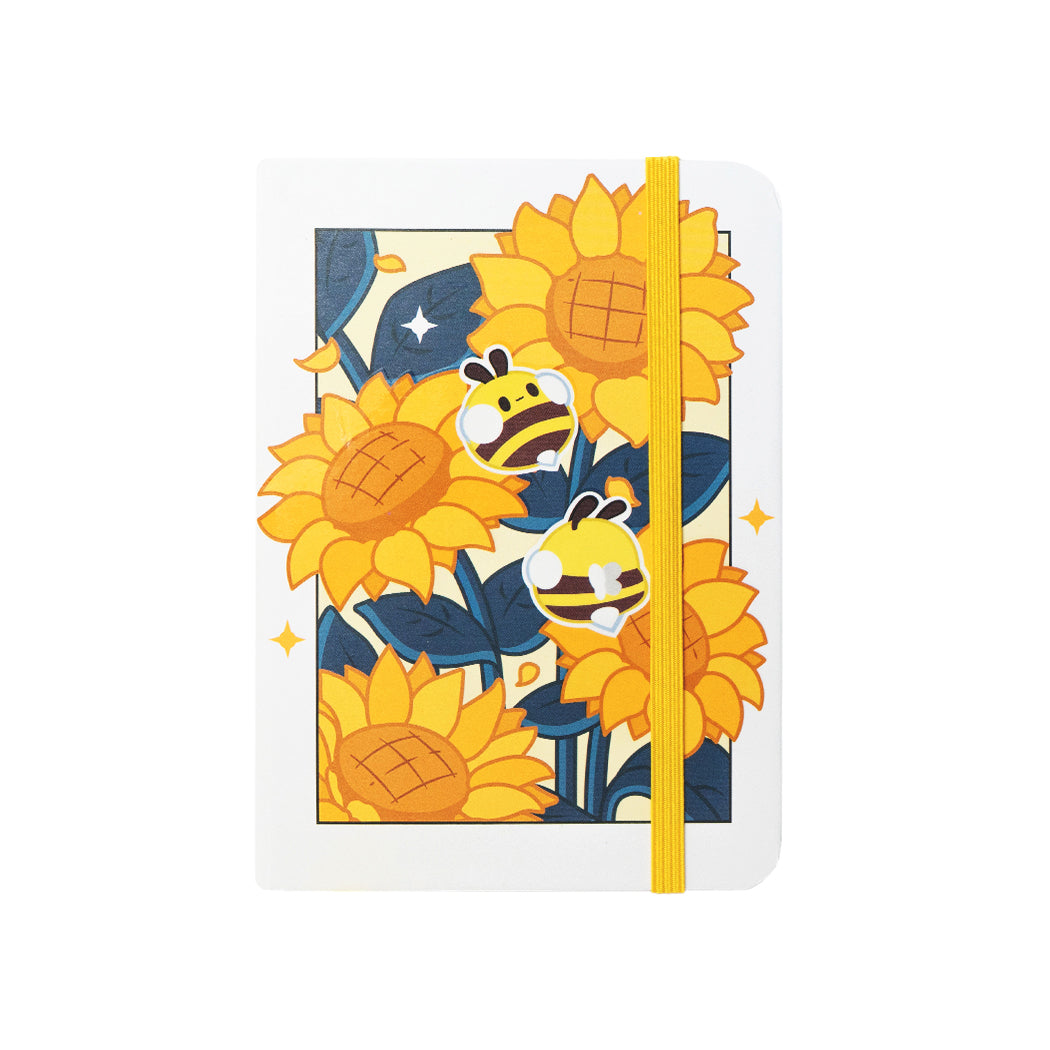 Notebook  formato A6 con copertina rigida e chiusura ad elastico. Sulla copertina e sul retro sono disegnati dei girasoli e delle apette.
