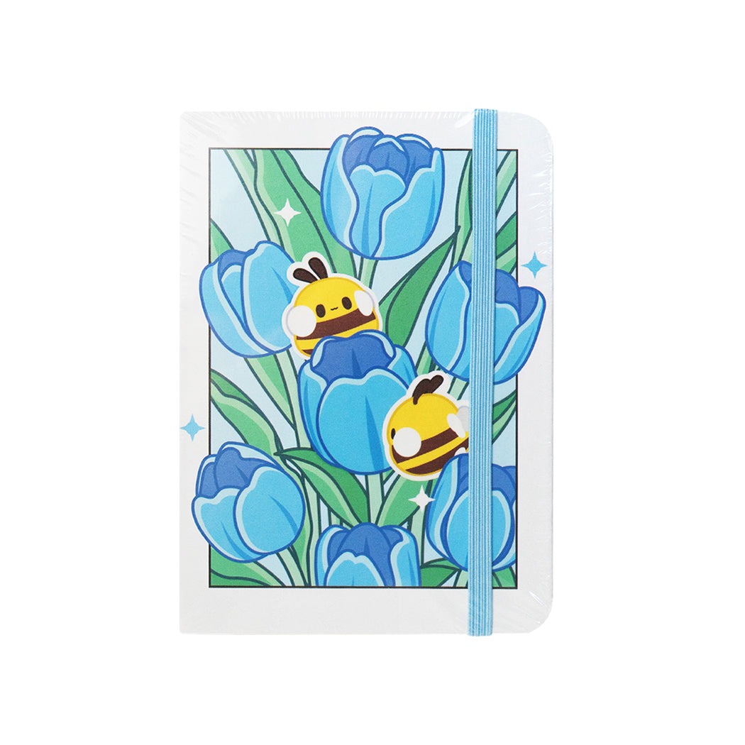 Notebook  formato A6 con copertina rigida e chiusura ad elastico.
Sulla copertina e sul retro sono disegnati dei tulipani blu e delle apette.