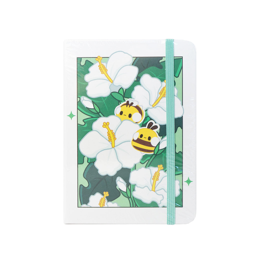 Notebook  formato A6 con copertina rigida e chiusura ad elastico.
Sulla copertina e sul retro sono disegnati dei fiori di hibiscus e delle apette.